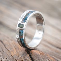 a silver ring with blue and green stones inlayed to the side on top of a piece of wood