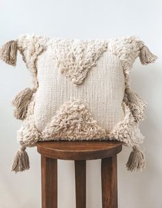 a white pillow with tassels sitting on top of a wooden stool