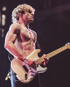 a shirtless man playing an electric guitar on stage