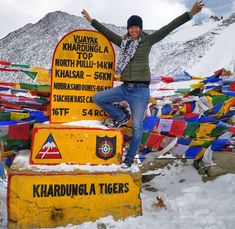 a woman standing on top of a sign in the snow with her arms up and hands out