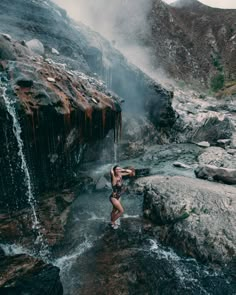 a woman standing in the water near a waterfall