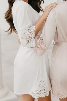 two women in white robes and one is holding the back of another woman's dress