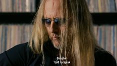 a man with long blonde hair and sunglasses looking at his cell phone in front of record shelves