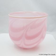 a pink glass bowl sitting on top of a white tableclothed surface with an abstract design in the center