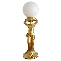 a golden statue holding a white ball on top of it's head and standing next to a lamp