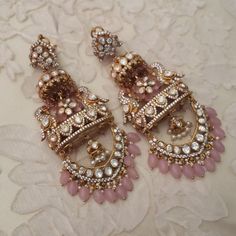 two pairs of pink and gold earrings on a white lace tablecloth with flowers in the background