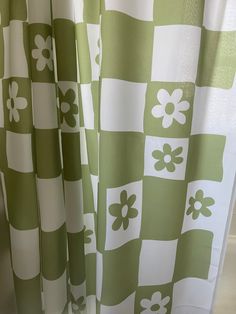 a green and white checkered shower curtain with flowers on the bottom, in front of a window