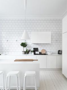 a white kitchen with lots of counter space and stools in front of the island