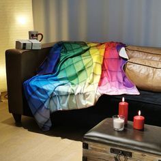 a couch with a rainbow blanket on top of it next to two candles and a coffee table