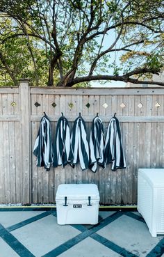 three coats hanging on a fence next to an ice chest