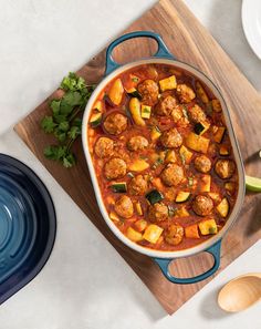 a pot filled with meatballs and vegetables on top of a wooden cutting board next to plates