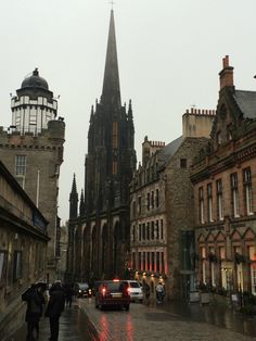 people are walking down the street in front of old buildings with an spire on top