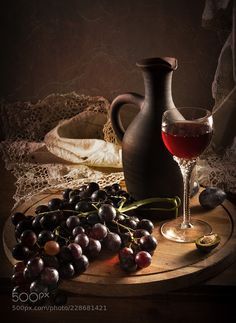 a glass of wine and some grapes on a wooden tray next to a jug with water in it