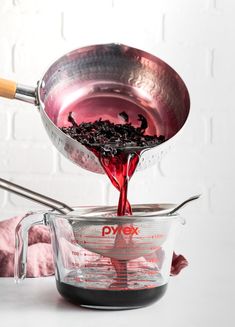 a person pouring red liquid into a bowl with a measuring cup in front of it