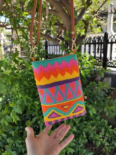 a hand holding a multicolored bag in front of a tree