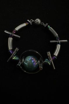 Experience the perfect fusion of futuristic vibes and avant-garde flair with our Planet Beaded Bracelet. At its center, the bracelet features a metal sphere surrounded by circular rings, resembling a celestial body. Interspersed along the bracelet are several elongated cylindrical beads, reminiscent of thorns, adding a touch of edginess to the design. In addition to the metal elements, the bracelet also features beads that reflect neon lights, creating a mesmerizing and futuristic effect. Crafte Modern Metal Beaded Bangle Bracelets, Modern Silver Beaded Bracelets, Silver Stainless Steel Beaded Bracelets, Modern Silver Bracelets With Silver Beads, Modern Handmade Silver Beaded Bracelets, Round Metal Bracelet With Silver Beads, Modern Silver Bracelet With Silver Beads, Unique Metal Bracelets, Silver Metal Bracelets With Spacer Beads