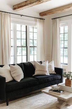 a living room filled with black couches and white drapes on the windowsill