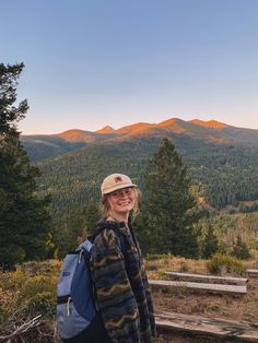 a woman standing on top of a wooden bench in front of some trees and mountains