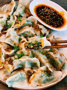 a plate full of dumplings with chopsticks on the side and sauce next to it