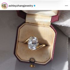 an engagement ring with a large diamond sits in a box on the table next to it