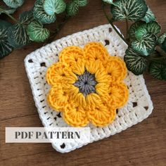 a crocheted square with a yellow flower on it and green leaves in the background