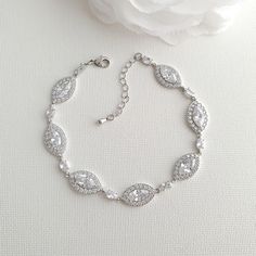 a white rose sitting on top of a table next to a bracelet with crystal stones