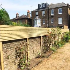 a wooden fence next to a brick wall in front of a house and some trees