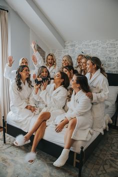 a group of women sitting on top of a bed in white bathrobe outfits