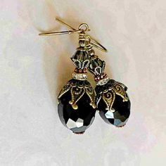 These bohemian black crystal dangle earrings are handmade with opaque faceted cut black crystals, and black diamond bi-cone shaped crystals.  Rustic boho black diamond crystal earrings are gracefully adorned in layers of Victorian style ornate antique gold plated brass bead caps and beads.   I set these steampunk inspired black crystal dangle earrings on antique gold plated brass ball tip hook ear wires.   ♛  Black is great to wear anytime and anywhere.  Black pairs well with indigo, midnight blue, emerald, gray, red, and yellow.   These fabulous black & antique brass gold earrings are the perfect gift for her, a friend, or treating yourself!  Simple Elegance. ♛ . . . ⚜️. Earrings Length: approx. 2" inches long ⚜️. Crystals : flat oval 16x14mm or 5/8" long & 1/2" wide ⚜️. Crystals : bicone Black Bohemian Earrings With Faceted Beads, Black Bohemian Teardrop Dangle Earrings, Black Teardrop Earrings With Black Beads, Black Faceted Bead Drop Earrings, Black Faceted Beaded Drop Earrings, Black Faceted Beads Earrings For Gift, Black Faceted Bead Earrings For Gift, Black Bohemian Earrings With Ear Wire, Handmade Black Bohemian Teardrop Earrings