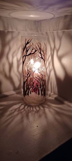 a lit candle is sitting on a table in the dark with trees casting long shadows