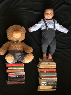 a baby laying on top of a pile of books next to a brown teddy bear