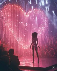 a woman walking down a runway in front of a heart - shaped stage with lots of lights