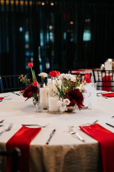 the table is set with red and white flowers, candles, and napkins on it