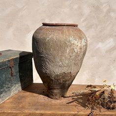 an old vase sitting on top of a wooden table next to a trunk and box