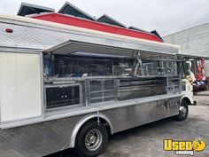 a silver food truck parked in a parking lot next to a building with red and white awnings