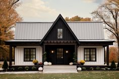 a black and white house with pumpkins on the front steps, trees in the background