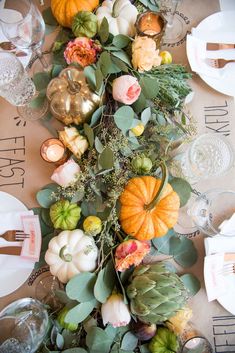 the table is set with pumpkins and greenery