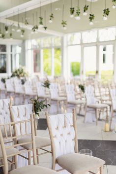 rows of chairs with white upholstered seats and greenery hanging from the ceiling