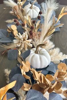 a wooden table topped with white pumpkins and blue leaves on top of it's sides