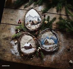 three small christmas ornaments are sitting on a wooden table next to fir branches and pine cones