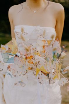 a woman in a white dress holding a bouquet of flowers with leaves on the side