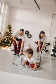 a man and woman with a baby on the floor in front of a christmas tree