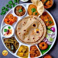 a plate filled with different types of food on top of a gray table next to bowls and spoons