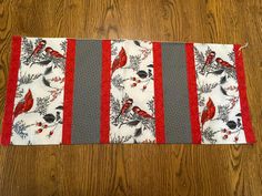 the table runner has red and gray birds on it, along with grey trimmings