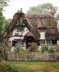 a white house with a thatched roof surrounded by greenery and flowers in the front yard