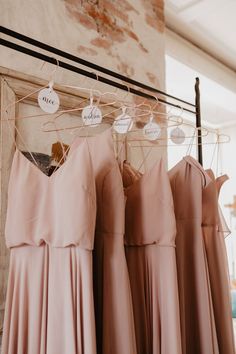 three bridesmaid dresses hanging on a rack in front of a brick wall with clothes hangers