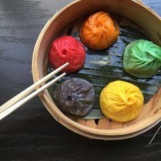 four different colored dumplings in a wooden bowl with chopsticks