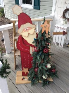 a santa clause sitting on top of a wooden chair next to a small christmas tree