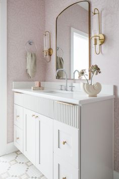 a white bathroom with pink wallpaper and gold accents on the mirror above the sink