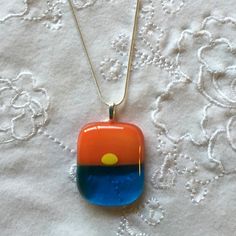 a necklace with an orange, blue and yellow design on it sitting on a white tablecloth